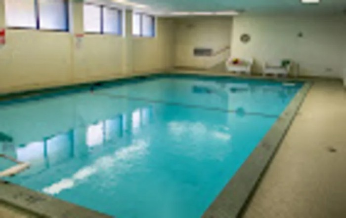 An indoor swimming pool with clear blue water, surrounded by beige walls and windows.
