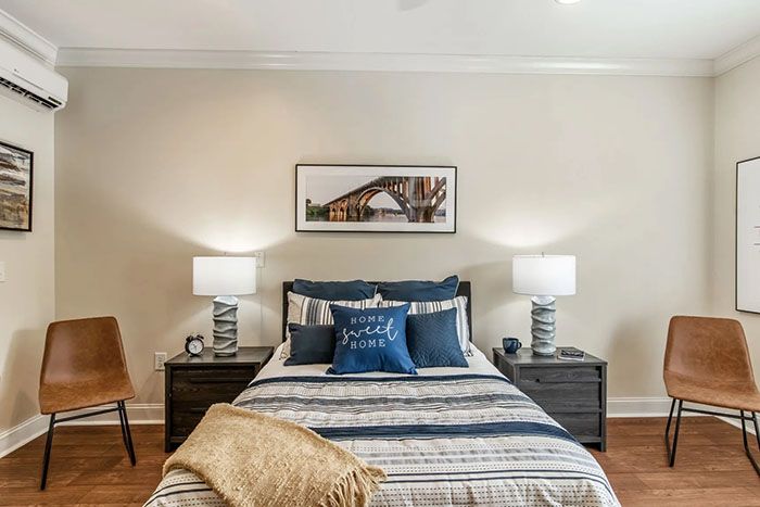 A cozy and well-decorated bedroom with a neatly made bed, flanked by two nightstands and lamps, featuring stylish wall art and decorative pillows.
