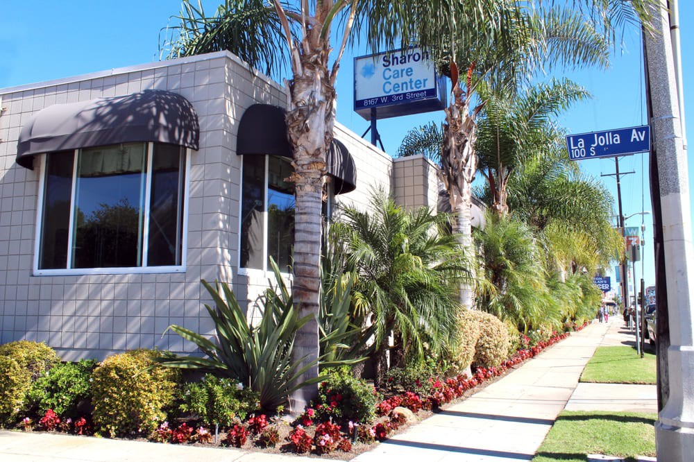 A well-landscaped building with palm trees and a sidewalk on a sunny day.