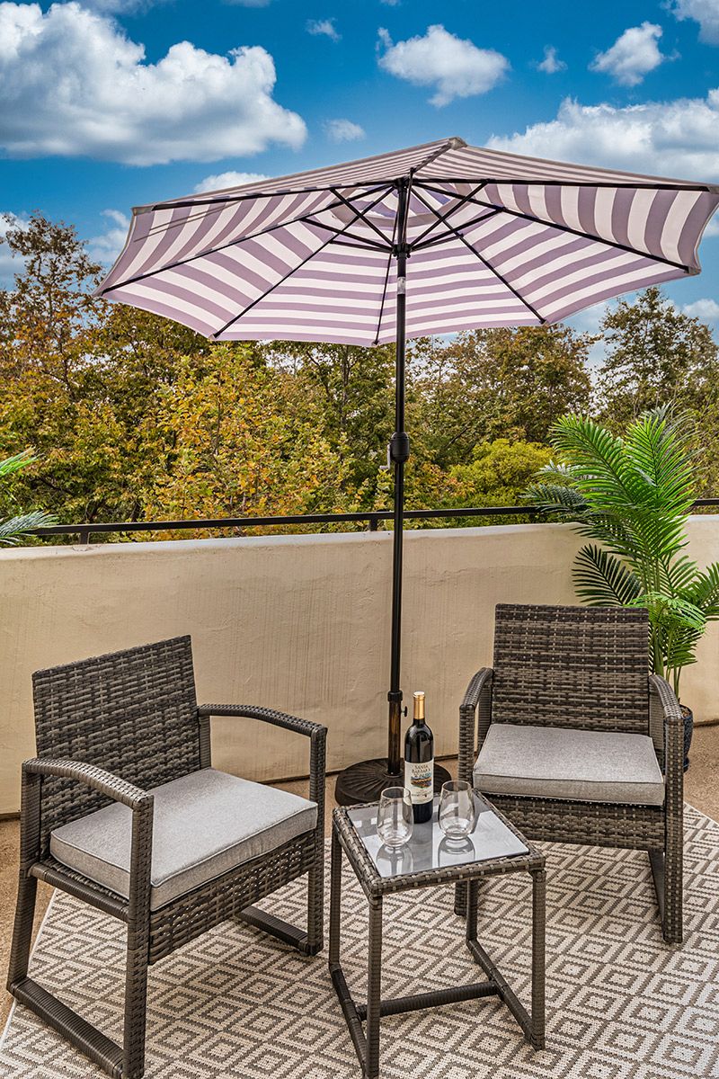 A cozy outdoor patio setup with wicker chairs, a small table, and a striped umbrella.