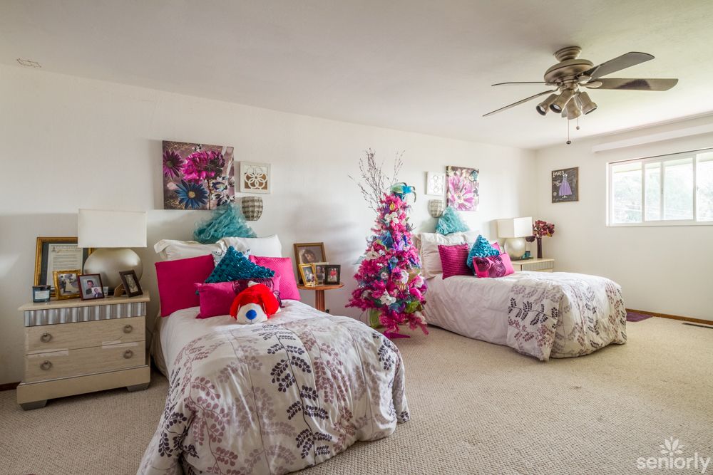 A vibrant bedroom with twin beds featuring colorful pillows and a festive Christmas tree in the corner.