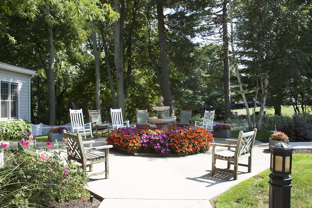 A well-arranged outdoor patio area with wooden chairs surrounding a central flower display, set amidst lush trees.