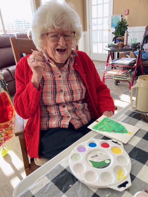 An elderly woman joyfully working on a painting project with art supplies.