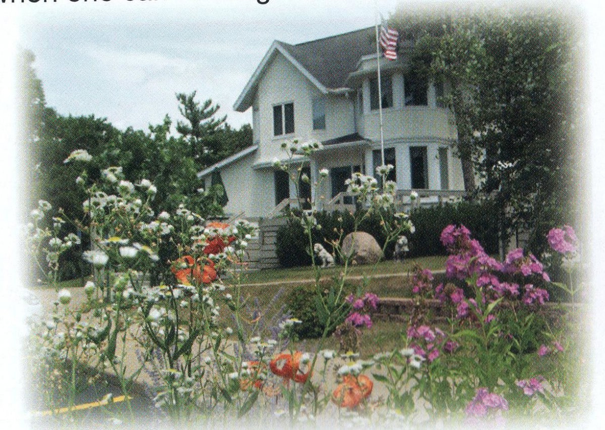 A charming house surrounded by a vibrant flower garden with an American flag flying in the yard.