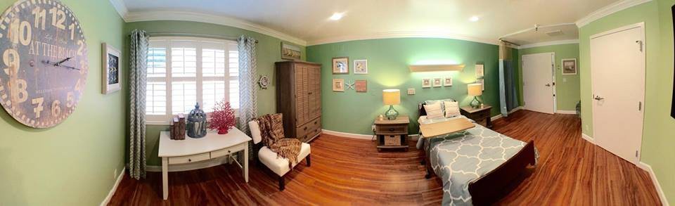 A cozy and well-decorated bedroom featuring green walls, wooden flooring, and a blend of furniture including a bed, wardrobe, lamp, and chair.