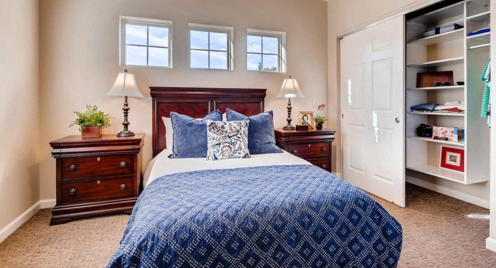 A cozy bedroom with a neatly made bed, blue bedding, and elegant wooden furniture.