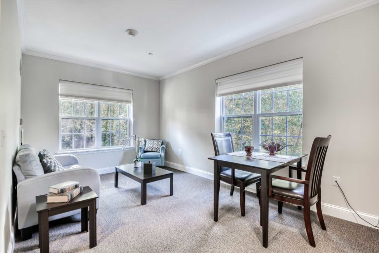 A modern living room with ample natural light, featuring cozy seating and a dining area.