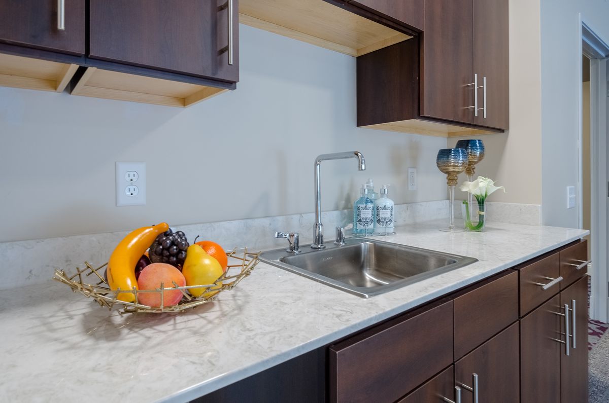 A modern kitchen with a clean countertop, featuring a fruit bowl and stainless steel sink.