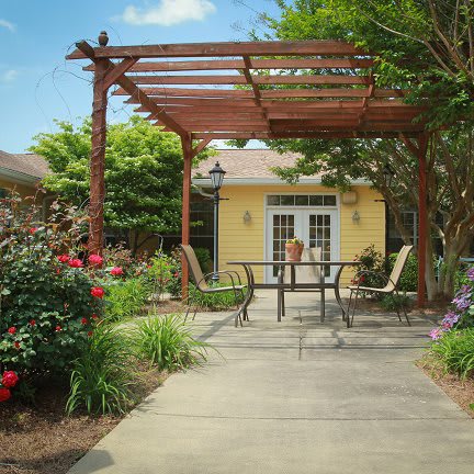 A beautiful garden patio with a wooden pergola, surrounded by vibrant flowers and greenery.