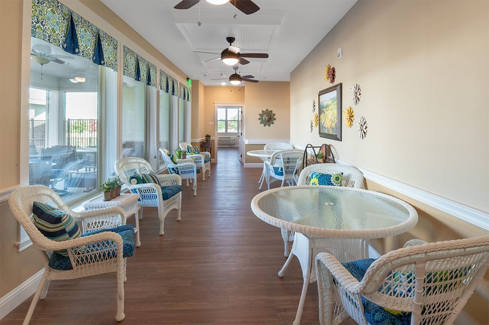 A cozy indoor seating area with tables and chairs, featuring large windows and ceiling fans.