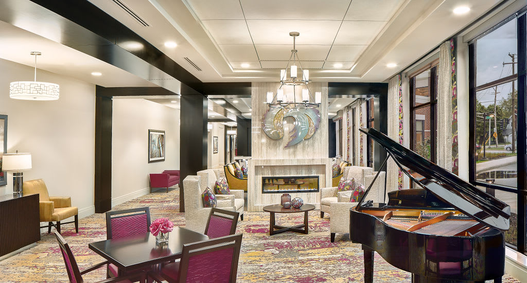 A luxurious living room featuring a grand piano, elegant furniture, and a modern fireplace with a chandelier overhead.