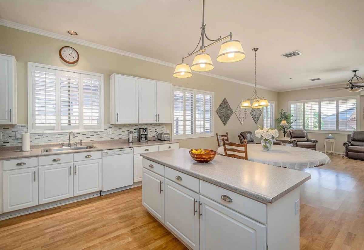 A modern kitchen with white cabinets and a central island, featuring wooden floors and pendant lighting.