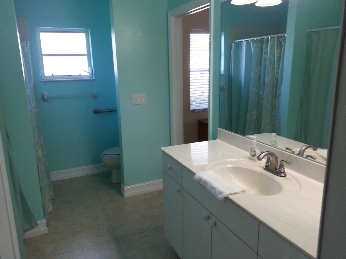 A clean and bright bathroom with turquoise walls, featuring a sink, mirror, toilet, and shower.