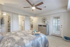A cozy bedroom featuring a ceiling fan, wooden dresser, and soft lighting.