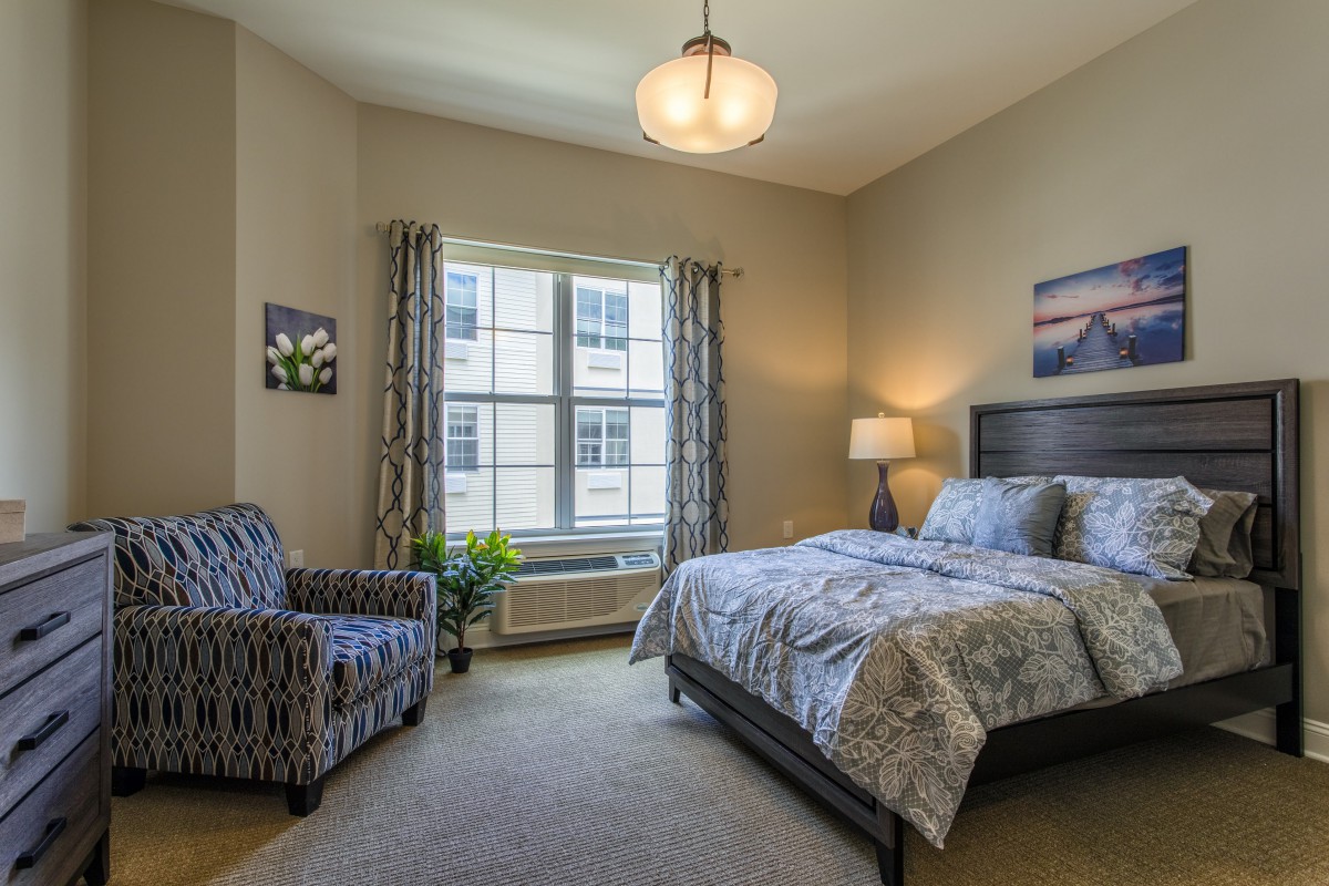 A cozy bedroom with a bed, armchair, and large window allowing natural light.