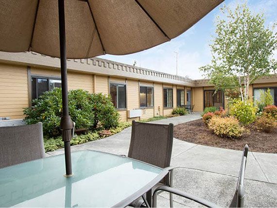 A tranquil outdoor patio area with a table, chairs, and an umbrella, surrounded by garden landscaping.