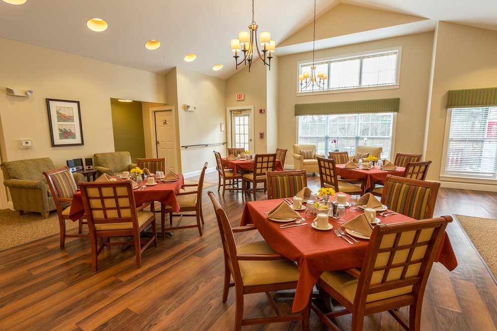 A cozy dining area with neatly arranged tables and chairs, featuring warm lighting and large windows.