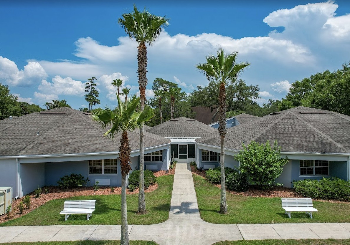 A building surrounded by palm trees with a neatly landscaped garden and pathway leading to the entrance.