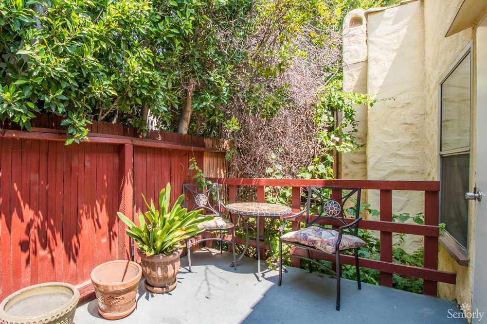 A small, sunny patio with a table and two chairs surrounded by lush plants.