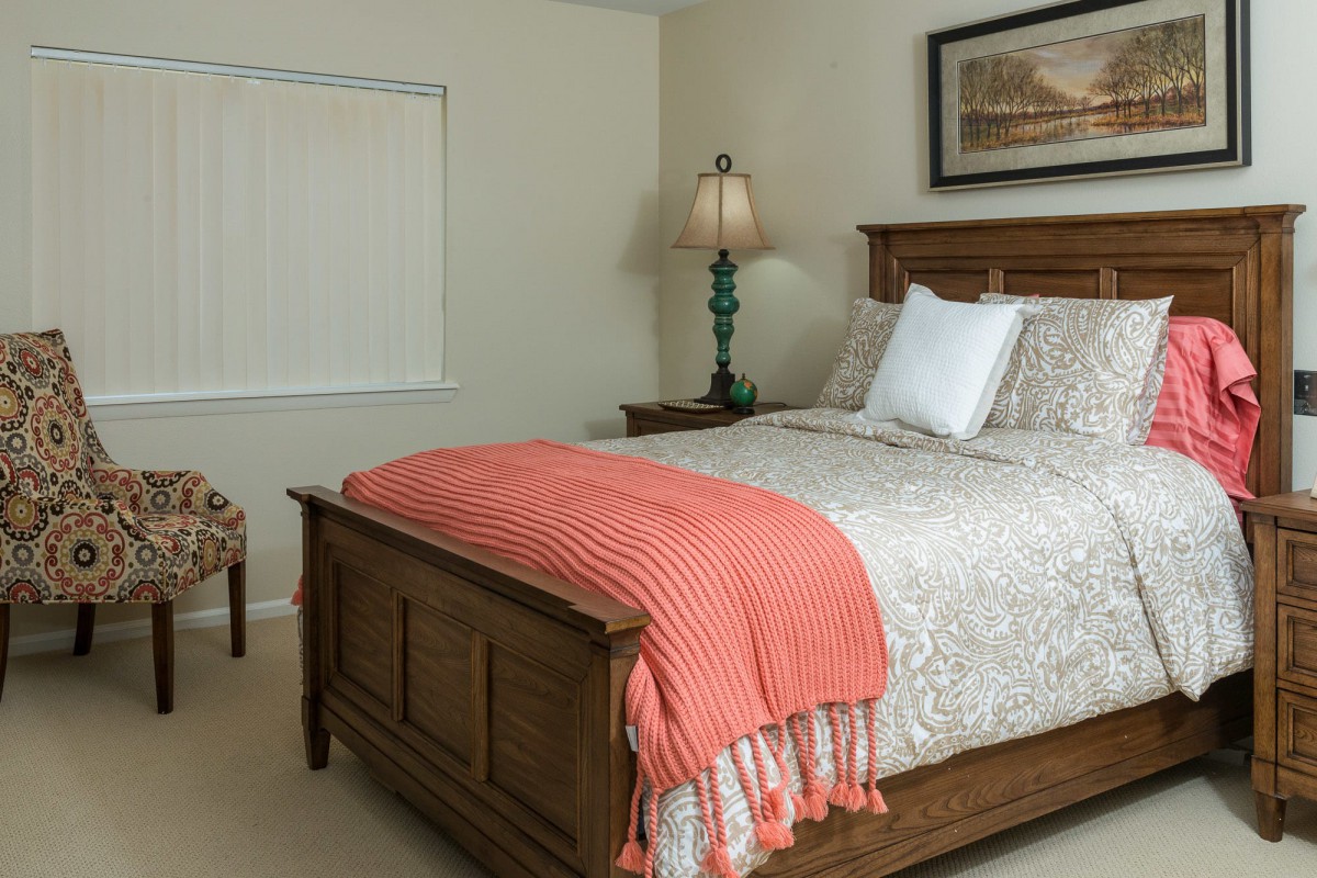 A cozy bedroom with a neatly made bed, featuring a colorful blanket and a bedside lamp.