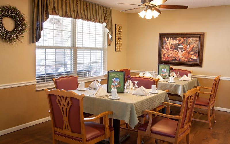 A well-decorated dining area with neatly arranged tables and chairs, featuring elegant table settings and wall art.