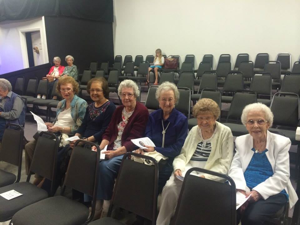 A group of elderly women seated in a row at an event.
