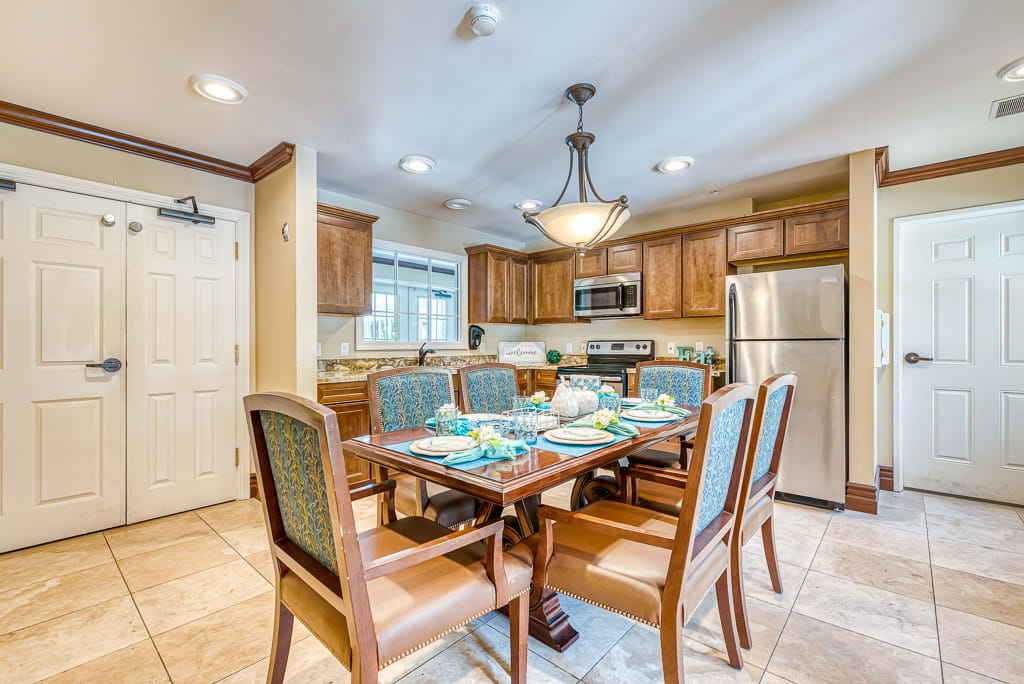 A modern kitchen and dining area with wooden cabinets, a dining table set for six, and stainless steel appliances.