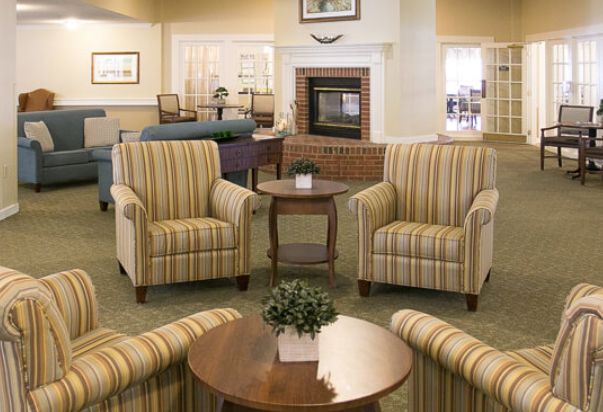 A cozy living room seating area with striped armchairs and coffee tables in front of a fireplace.