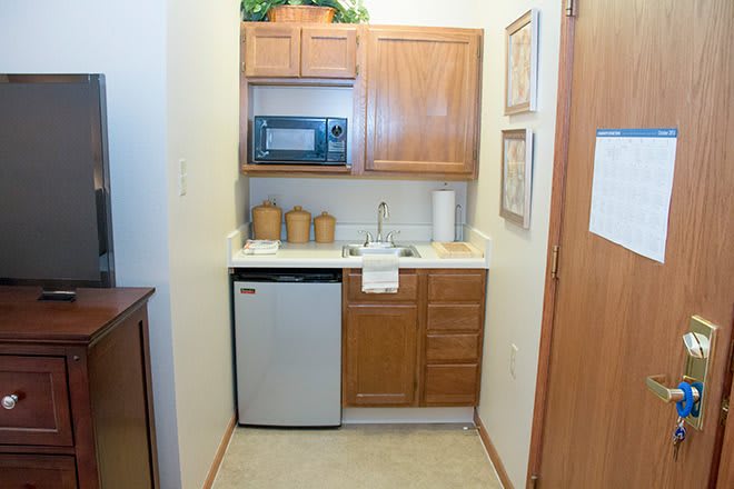 A compact kitchenette featuring a microwave, sink, mini fridge, and wooden cabinets.
