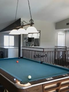 A spacious recreational room featuring a pool table under stylish lighting.