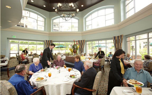 A group of people dining in a well-lit restaurant setting, with waitstaff attending to them.