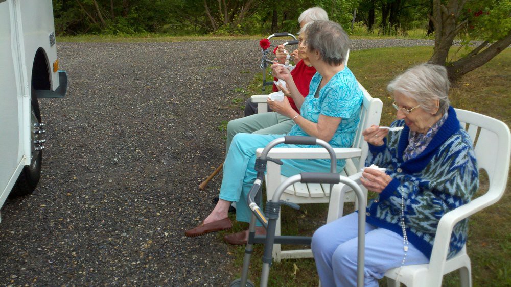 A group of seniors sitting in chairs outdoors, enjoying a leisurely moment with their walkers nearby.