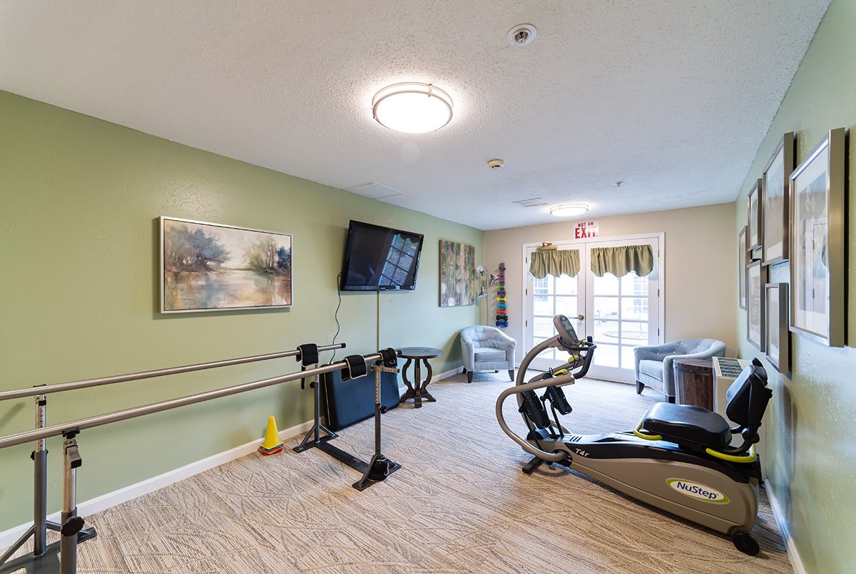 A modern exercise room equipped with a treadmill, stationary bike, and television, featuring wooden floors and large windows.