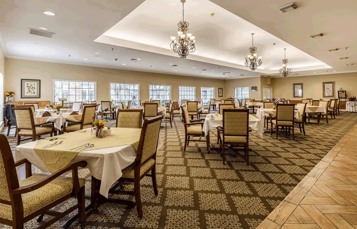 An elegant dining room with neatly arranged tables and chairs, featuring chandeliers and large windows.
