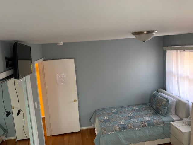 A minimalist bedroom featuring blue walls, a bed with patterned covers, and a small window.