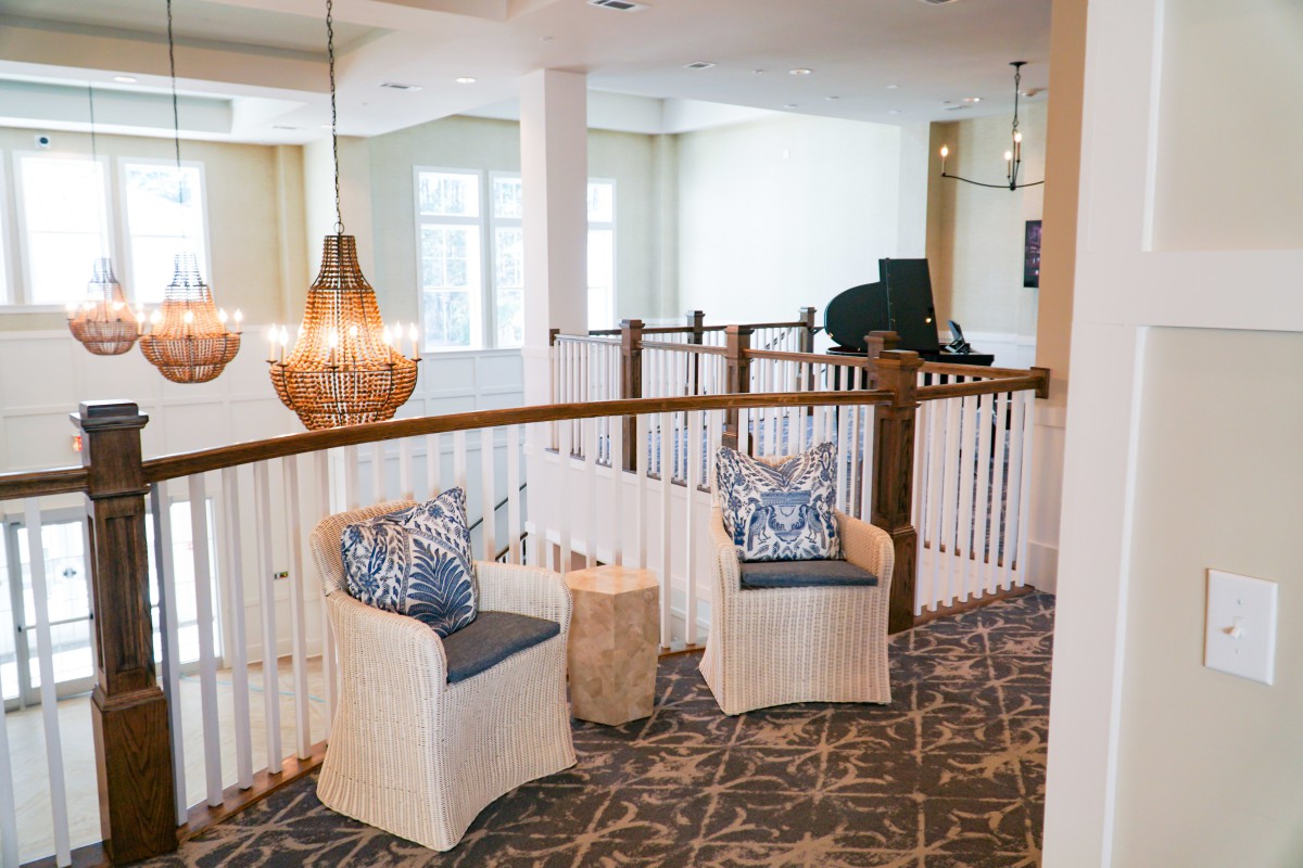 A cozy seating area on an interior balcony features stylish chairs, decorative cushions, and a chic chandelier.