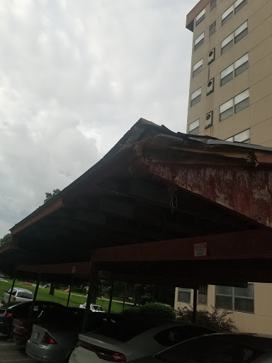 A weathered carport structure with a building in the background under a cloudy sky.