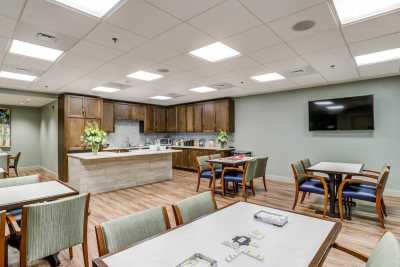 A well-lit dining and kitchen area with tables, chairs, and a mounted television.