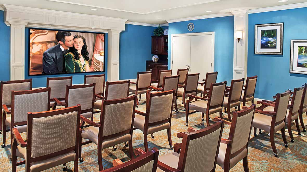 An empty meeting room with rows of chairs facing a projector screen.