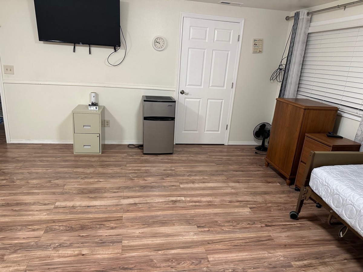 A tidy room with wooden flooring, featuring a mounted television, a small cabinet, and a door.