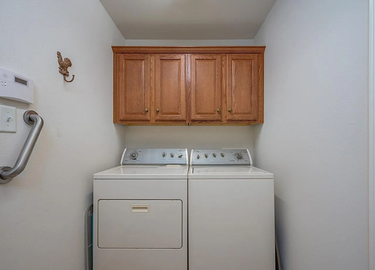 A compact laundry room with a washing machine and dryer beneath wooden cabinets.