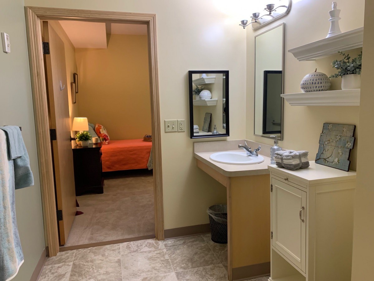 A view from a bathroom into a bedroom with warm lighting and simple decor.