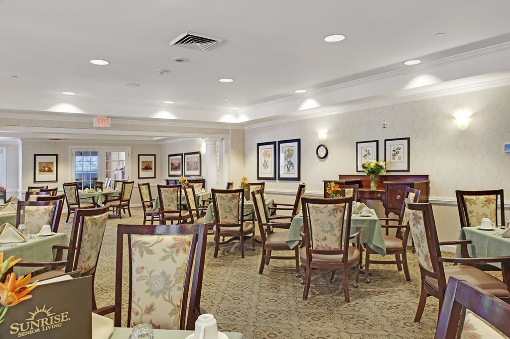 A well-lit dining area with multiple tables and chairs arranged neatly, featuring elegant decor and carpeted flooring.
