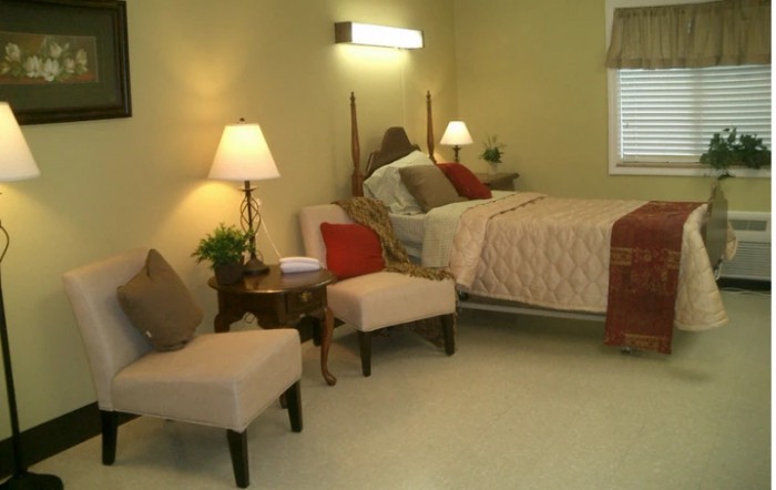 A cozy bedroom with a bed, two chairs, and soft lighting.