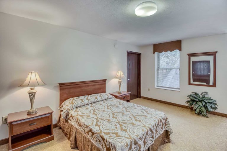 A cozy bedroom with a neatly made bed, nightstands, and a window providing natural light.