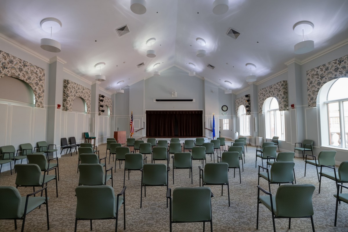 An empty auditorium with rows of chairs facing a stage.