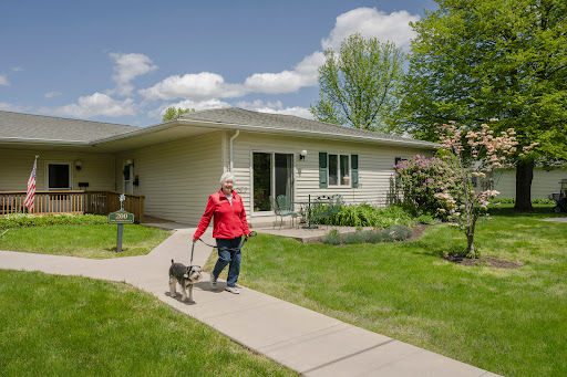 A woman walking her dog along a pathway in front of her house on a sunny day.
