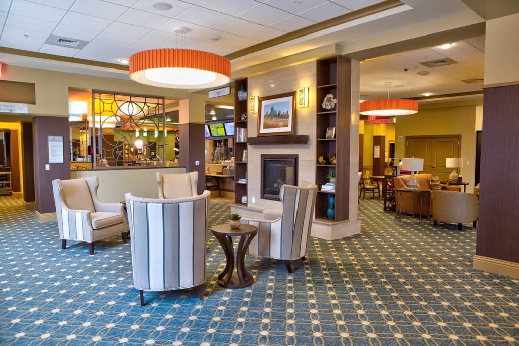A modern hotel lobby featuring a cozy seating area with striped chairs, a central fireplace, and stylish lighting.