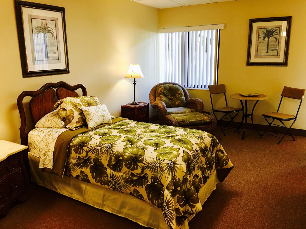A cozy bedroom with a single bed, an armchair, and a small table near a window.