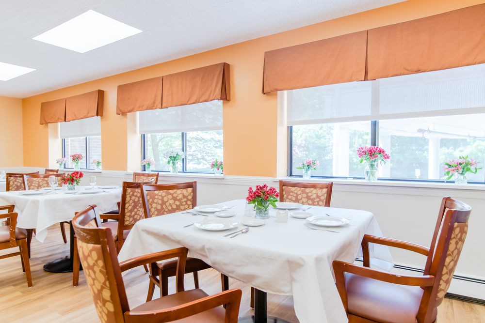 A bright and well-lit dining room with elegantly set tables, adorned with flowers.